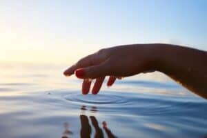 A woman's hand hovers over water, as she dips her fingers into the surface of the water.