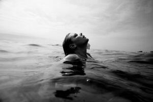 A woman who is swimming in a body of water tilting her head back to look at the sky.