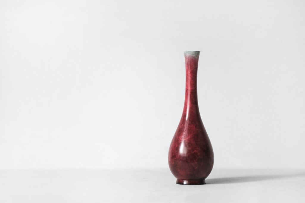 Reddish vase on a white surface in a white room.